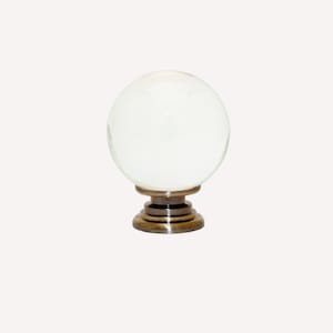 Peut inclure: Un bouton de porte en verre transparent avec une base en laiton. Le bouton est rond et a une surface lisse. La base est un design simple avec un dessus plat et un fond légèrement évasé.