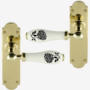 May include: Two brass door handles with white ceramic knobs featuring black floral designs. The handles are rectangular with rounded edges and have a polished finish.