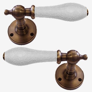 May include: Two antique brass door handles with white ceramic lever handles. The handles have a round base with two screw holes.