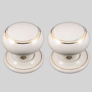May include: A pair of white ceramic door knobs with gold detailing. Each knob features a rounded top with a gold band and a matching gold trim on the base. These knobs are designed for interior doors.