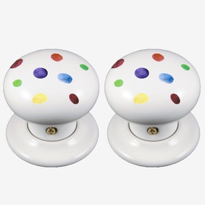 May include: Two white ceramic door knobs with colourful polka dots. The knobs have a round shape and a flat base.