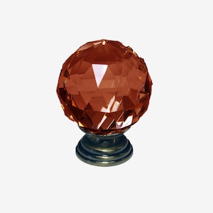 Puede incluir: Un pomo de armario redondo de cristal facetado de color ámbar con una base de níquel cepillado.