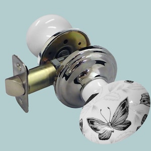 May include: A white porcelain door knob with a butterfly design. The knob is attached to a chrome door handle with a brass latch.