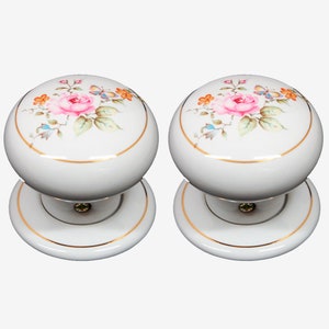 May include: Two white ceramic door knobs with a gold trim and a floral design featuring pink roses, butterflies, and green leaves.