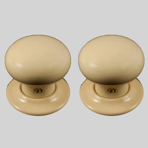 May include: Two off-white ceramic door knobs with a round shape and a flat base. The knobs have a small gold screw in the center.