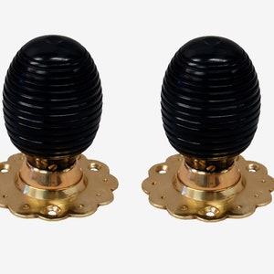 May include: Two black wooden door knobs with gold metal bases and decorative edges. The knobs have a ribbed design.