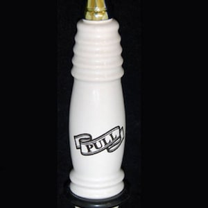 May include: White ceramic toilet pull handle with a black banner that says "PULL" in a vintage font. The handle has a gold colored top.