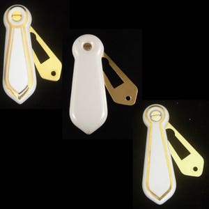 May include: Three white ceramic door knob covers with gold trim and a gold keyhole. The covers are shaped like a tie.