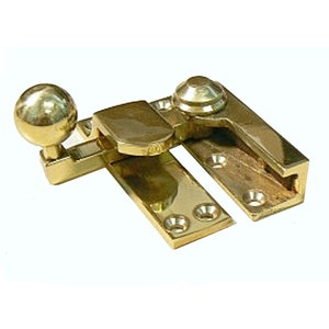 May include: A polished brass window latch with a round knob. The latch has a rectangular base and a lever that can be moved to lock or unlock the window.