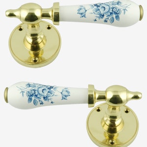 May include: A pair of brass door handles with white ceramic levers featuring a blue floral design. The handles have a round base with screw holes.