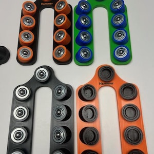 Op de afbeelding: Een verzameling kleurrijke batterij-organizers in zwart, oranje en groen. Elke organizer bevat meerdere batterijen, met het woord "Hammer" op sommige gedrukt. De batterijen zijn zilver, oranje en blauw.