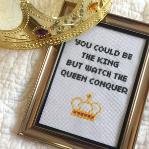 May include: A framed cross-stitch with the text "You could be the king but watch the queen conquer" and a yellow and red crown design.