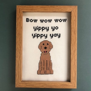 Puede incluir: Un bordado enmarcado con un perro marrón y el texto "Bow wow wow yippy yo yippy yay".