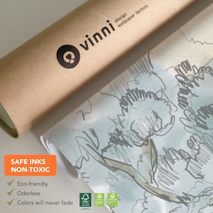 Op de afbeelding: Een rol behang met een lichtblauwe achtergrond en een grijs en groen bloemenpatroon. Het behang is gelabeld "vinni design wallpaper factory". De tekst "SAFE INKS NON-TOXIC" staat op een groen label met een vinkje naast de woorden "Eco-friendly", "Odorless" en "Colors will never fade".
