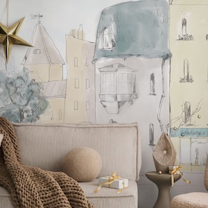 Op de afbeelding: Een woonkamerinterieur met een beige bank en een bruin gebreid deken. De muur achter de bank heeft een handgetekend muurschildering van een straat in de stad met gebouwen en een boom. Er hangt een gouden ster aan het plafond.