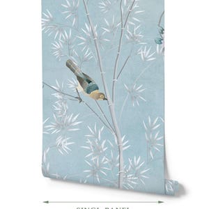 Puede incluir: Un rollo de papel tapiz con fondo azul claro, tallos de bamb&uacute; blancos y un p&aacute;jaro con plumas marrones, azules y grises. El texto en la parte inferior indica un ancho de panel &uacute;nico de 61 cm, mostrado con una flecha de medici&oacute;n doble.