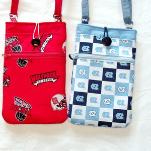 May include: Two fabric zippered pouches with adjustable straps. The red pouch has a basketball and a wolfpack logo with the text "NC State". The blue pouch has a checkered pattern with the text "UNC" repeated.