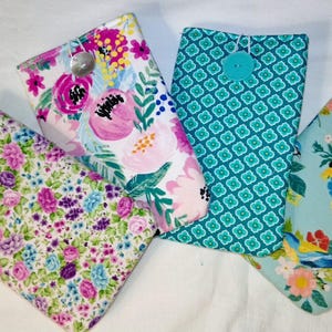 May include: Four rectangular fabric pouches with button closures. One features a small floral print, another a large pink and white floral pattern, the third a teal geometric design, and the fourth a light blue fabric with birds and flowers.
