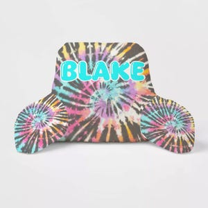 May include: A tie-dye patterned reading pillow with a blue "BLAKE" name in bubble letters. The pillow has two smaller tie-dye patterned pillows attached to the back.