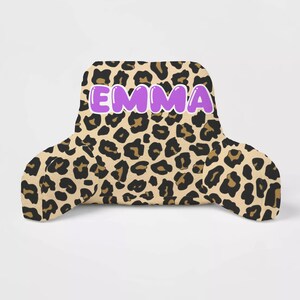 May include: A brown and black leopard print reading pillow with the name "EMMA" in purple bubble letters.