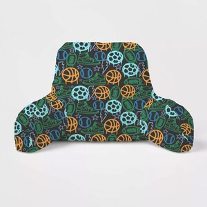 May include: Black backrest pillow with a repeating pattern of sports equipment, including basketballs, soccer balls, footballs, and sneakers in neon green, orange, and blue. The pillow has a curved shape for back support.