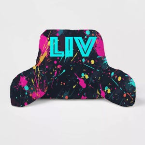 May include: A black and blue reading pillow with a colorful paint splatter design. The pillow has the word "LIV" printed in turquoise on the front.