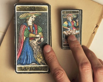 Puede incluir: Dos cartas de tarot, una con una mujer con un vestido azul y verde sosteniendo un león, y la otra con un hombre con un atuendo colorido sentado en una mesa. La carta con la mujer tiene el texto "LA FORCE".