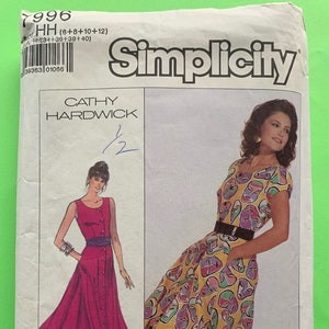 Può includere: Modello di cucito Simplicity con due modelli di abiti. Uno è un abito abbottonato color magenta con cintura blu navy. L'altro abito è giallo con un motivo di maschere colorate. Il modello include il nome "Cathy Hardwick".