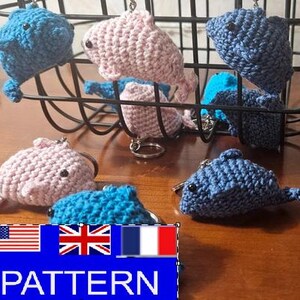 May include: Crocheted whale keychains in shades of blue and pink are displayed. The handmade keychains have black button eyes and silver key rings. The word "PATTERN" is visible in a blue rectangle with the American, British, and French flags.