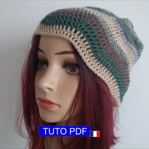 May include: A crocheted beanie hat with stripes of beige, green, brown, and blue. The hat is on a mannequin head with long, dark red hair. The text "TUTO PDF" is on a blue rectangle with a French flag.