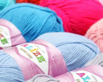 May include: Close-up of colorful yarn skeins in shades of blue, pink, orange, and gray. The yarn is labeled "Alize Cotton Gold". Ideal for knitting and crochet projects.