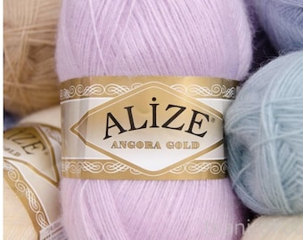 May include: Close-up of several skeins of Alize Angora Gold yarn in various pastel colors. The main skein is a soft lavender with a gold label. Other colors include light blue and beige. Ideal for knitting and crochet projects.