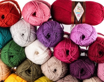 May include: A pile of colourful yarn balls in shades of red, pink, teal, green, and purple. A single skein of red yarn with a label is also present. Suitable for knitting and crochet projects.