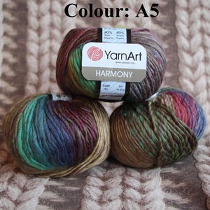 May include: Three balls of YarnArt Harmony yarn in colour A5. The yarn is a blend of wool and acrylic, with a mix of colours including brown, green, blue, and red. The label indicates the yarn composition and brand.