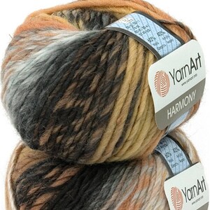 May include: Two balls of YarnArt Harmony yarn, colour A13. The yarn is a mix of brown, tan, grey, and peach shades. Each ball has a label with the brand name and fibre content. The text "Colour: A13" is at the top.