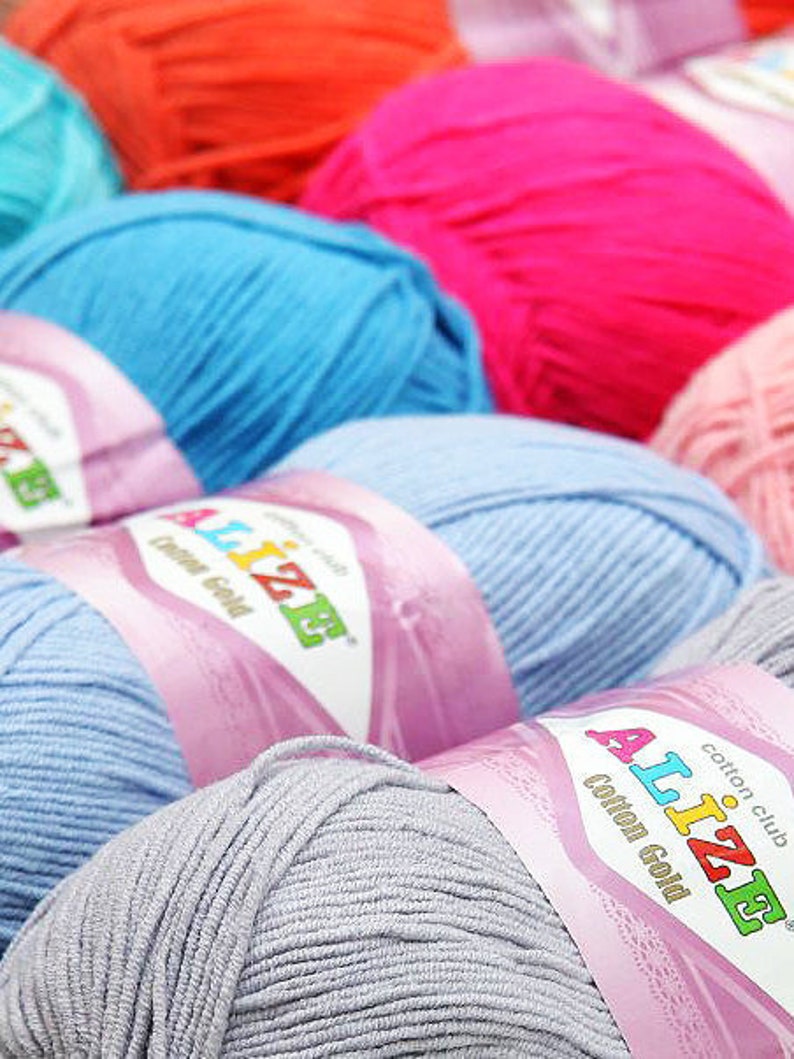 May include: Close-up of colorful yarn skeins in shades of blue, pink, orange, and gray. The yarn is labeled "Alize Cotton Gold". Ideal for knitting and crochet projects.