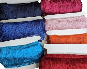 May include: Assortment of fringe trim in various colors, including purple, navy blue, royal blue, pink, orange, turquoise, and red. The fringe is displayed on white card stock.