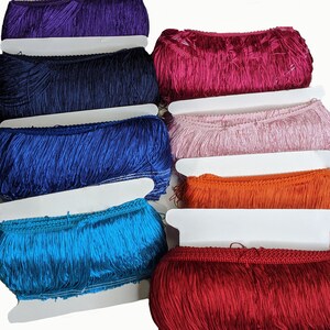 Op de afbeelding: Assortiment van franjes in verschillende kleuren, waaronder paars, donkerblauw, koninklijkblauw, roze, oranje, turquoise en rood. De franjes worden gepresenteerd op wit karton.