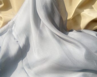 Puede incluir: Primer plano de tela drapeada en tonos azul claro y amarillo pálido. La tela es suave y fluida, con pliegues y sombras visibles que crean una sensación de profundidad y textura. La tela azul claro está en primer plano, mientras que la tela amarilla está en el fondo.