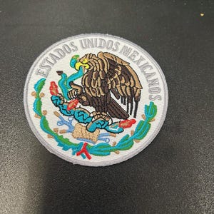 May include: A white embroidered patch with the text "Estados Unidos Mexicanos" in a circle around a colorful image of an eagle with a snake in its talons.