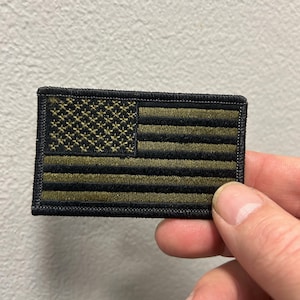 以下が含まれることがあります： 黒と緑の刺繍が施された小さなアメリカの旗のパッチ