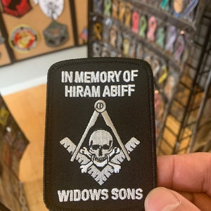 May include: Black embroidered patch with white text that reads "In Memory of Hiram Abiff Widows Sons". The patch features a white skull and crossbones with a compass and square above it.