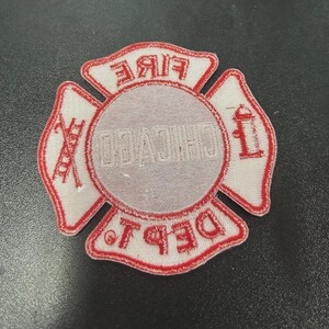 Pu&ograve; includere: Una toppa ricamata bianca e rossa a forma di croce di Malta. Il centro presenta la scritta CHICAGO, mentre le sezioni superiore e inferiore riportano FIRE e DEPT. Le sezioni laterali mostrano una scala e un idrante ricamati.