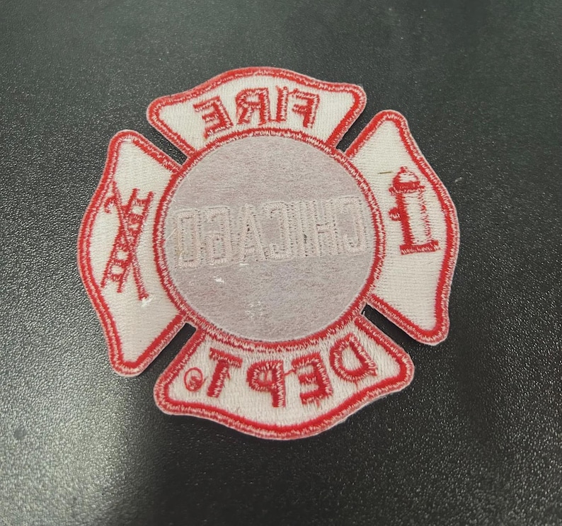 Pu&ograve; includere: Una toppa ricamata bianca e rossa a forma di croce di Malta. Il centro presenta la scritta CHICAGO, mentre le sezioni superiore e inferiore riportano FIRE e DEPT. Le sezioni laterali mostrano una scala e un idrante ricamati.