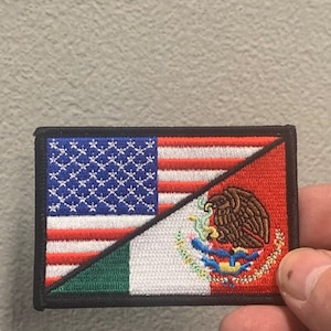 May include: A patch with the American and Mexican flags sewn together. The American flag is on the left side of the patch and the Mexican flag is on the right side. The flags are sewn together in a diagonal pattern. The patch is made of fabric and has a black border.