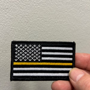 Op de afbeelding: Een zwart-wit Amerikaanse vlag patch met een dunne gele streep in het midden. De patch is geborduurd en heeft een zwarte rand.