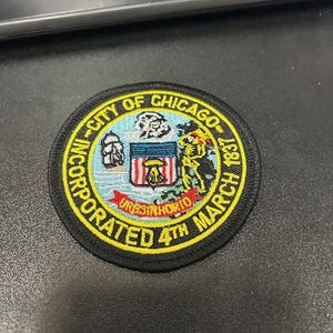 May include: Black and yellow embroidered patch with the text "City of Chicago Incorporated 4th March 1837" and a stylized image of a coat of arms.