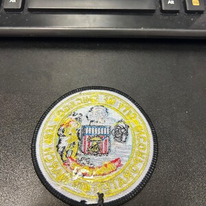 May include: A white and yellow embroidered patch with a black border. The patch features a shield with a red, white, and blue design and the text "CHICAGO POLICE DEPARTMENT" around the shield.