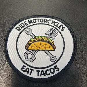 May include: White embroidered patch with black border. The patch features a crossed wrench and piston with a taco in between. The text "Ride Motorcycles Eat Tacos" is written around the edge.