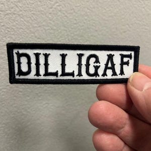 May include: White patch with black embroidered text that reads "DILLIGAF".